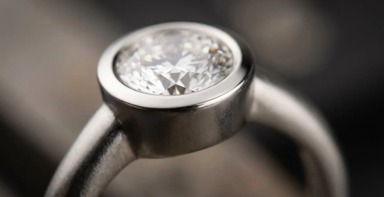 Extreme Nahaufnahme einer Diamantfassung mit sichtbaren Metalldetails und Oberflächentextur, die den Unterschied zwischen einer glatten Zargenfassung und einer riskanten Krappenfassung zeigt.