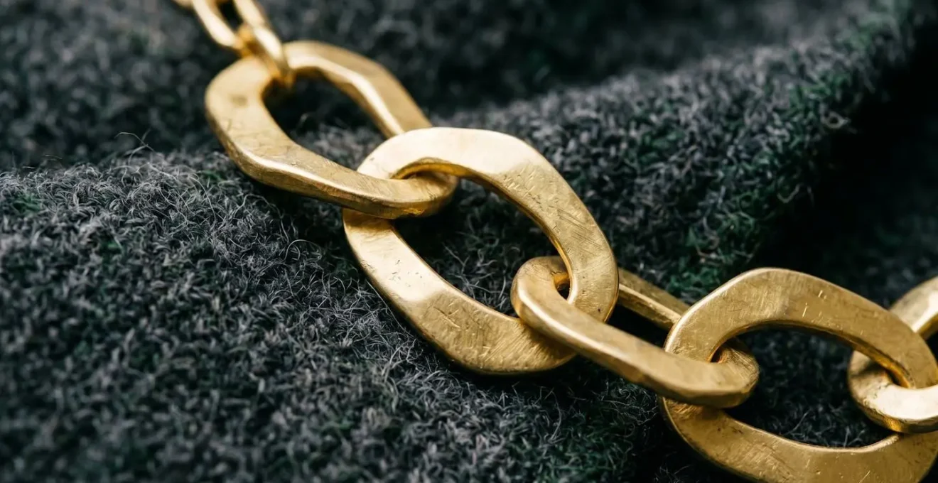Nahaufnahme von poliertem Goldschmuck auf mattem Wollstoff mit texturalen Kontrasten
